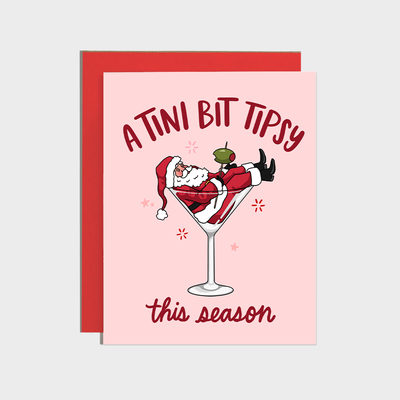 The Martini Tipsy Santa Holiday Card by Brittany Paige features Santa in a martini glass with "A Tini Bit Tipsy" above and "this season" below. This A2 card has high quality paper, a matching red envelope, and a cheerful pink background.