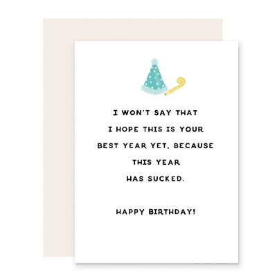 The Wont Say Best Year Ever Birthday Card by Slightly Stationery is an A2 cream cardstock card featuring a party hat and noisemaker, with the message: I won’t say that I hope this is your best year yet, because this year has sucked. Happy Birthday!”.
