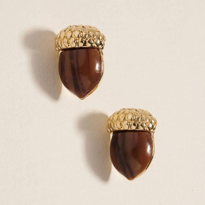 Sensibling Corp.’s Acorn Stud Earrings, featuring textured gold tops and glossy brown bottoms, are hypoallergenic with titanium post backs for comfort, displayed on a light neutral background.