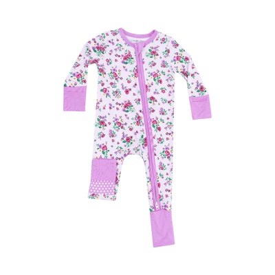 The Preppy Roses Two-Way Zipper Romper by Angel Dear is a white bamboo fiber onesie with a floral pink and purple pattern. Ideal for sensitive skin, it features lavender cuffs, feet, and a vertical zipper to one leg. The left knee has a patch with white polka dots.