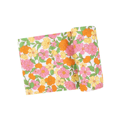 The vibrant design of the Angel Dear Botanical Retro Floral Muslin Swaddle Blanket features a colorful array of orange, pink, and yellow flowers with green leaves on a white background, offering a touch reminiscent of floral-patterned wrapping paper.