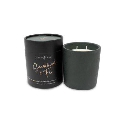 The Earth & Ember 13 oz Candle: Sandalwood & Fir by Milkhouse Candle Company features a black jar with white soy wax and comes in a matching black cylindrical container—an elegant gift for any occasion.