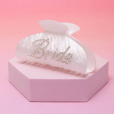 The SP Sophia Collection Bride Rhinestone Embellished White Pearlescent Hair Clip is displayed on a pale pink hexagonal platform with a pink gradient background.