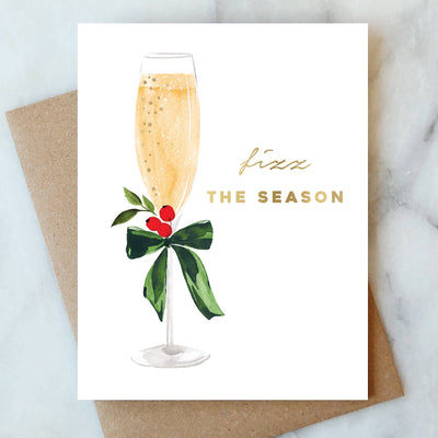 The Abigail Jayne Design Fizz the Season Holiday Greeting Card box set features 6 cards with a watercolor champagne glass, green leaves, red berries, and gold "fizz THE SEASON" text, each displayed with a brown envelope.