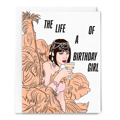 A glamorous woman in a beaded headpiece and feathers holds a cocktail with bold text: The life of a birthday girl. The Life of a Birthday Girl TS Showgirl Card by Sammy Gorin LLC is an A2 folded card with blank envelope.