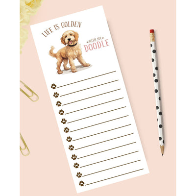 The Stylish Scribe’s Doodle Dog notepad features cute doodle dog art, “Life is golden with my doodle” text, paw prints beside each line, heavy smooth white paper, plus a polka dot pencil and gold paperclips on a pale pink background.