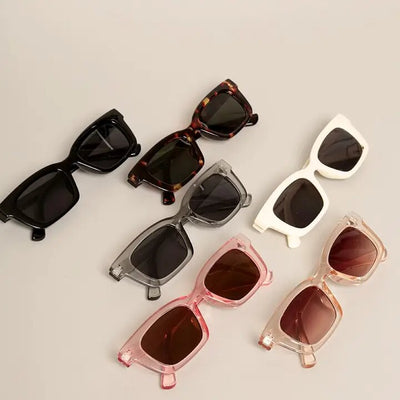 Six pairs of Fashion Citys Lola Sunglasses are elegantly displayed on a plain surface, highlighting square frames in black, tortoiseshell, white, transparent gray, pink, and transparent beige—all offering UV400 protection for optimal sun safety.