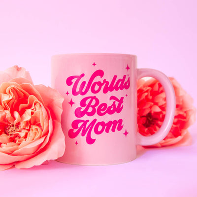 The Worlds Best Mom Mug by Sunshine Studios features a pink ceramic design with Worlds Best Mom in bold pink cursive, surrounded by soft pink roses against a matching backdrop, creating a warm and celebratory gift for mothers.