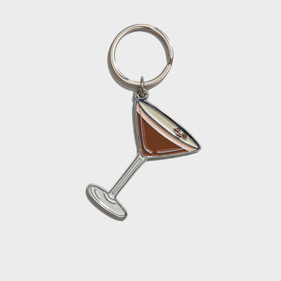 The Brittany Paige Espresso Martini Enamel Keychain features a martini glass charm with brown liquid, making it a perfect coffee lover gift. It’s attached to a metal keyring and displayed on a light background.
