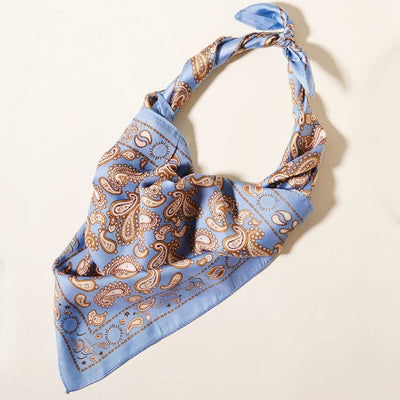 The Paisley Printed Square Silky Satin Scarf by Sensibling Corp. features a light blue base with brown and ivory paisley patterns, tied in a knot at one end and displayed on a pale surface.