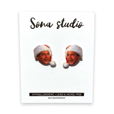 Clark Christmas Earrings by Sona Studio feature a man's smiling face in a Santa hat, on a card labeled Hypoallergenic • Lead & Nickel Free • Not Waterproof. Perfect festive earrings for sensitive ears.