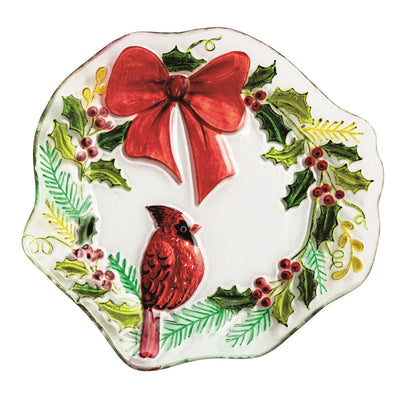 The Mud Pie Cardinal Wreath Plate is a hand-painted glass platter with a scalloped edge, featuring a red cardinal on a branch amid holly leaves, red berries, pine sprigs, and topped with a vivid red bow.