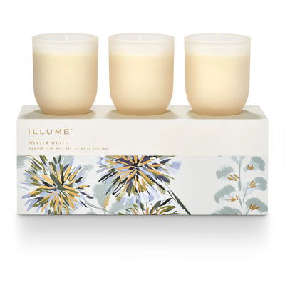 The Illume Candles Winter White Candle Trio Gift Set features three white plant-based wax candles in frosted glass holders, elegantly displayed in a decorated floral box with the product name.