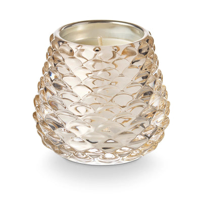 The Illume Candles Winter White Pinecone Votive Candle features a decorative glass holder with a metallic interior and a textured, pinecone-inspired pattern, plus a single white wick in the center.