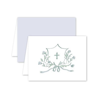 The Avonlea Periwinkle Cross Greeting Card by Dogwood Hill showcases folded cards with a floral illustration featuring a central cross and shield shape on Mohawk Eggshell White Paper. Pastel blue and white tones add softness, paired with an elegant Euro flap envelope.