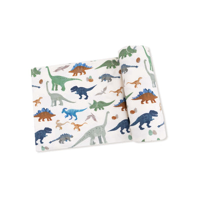 The Washy Dinos Bamboo Stretch Knit Swaddle Blanket by Angel Dear features colorful dinosaur and egg illustrations on a white background. Made of soft bamboo fabric, this swaddle is partially rolled up in the image.