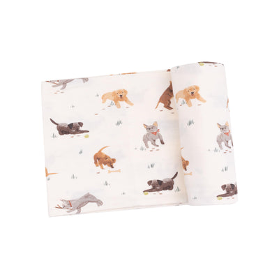 The Angel Dear Watercolor Puppies Bamboo Stretch Knit Swaddle Blanket features a playful pattern of cartoon dogs running, playing with balls, or standing on a white background with small grass patches.