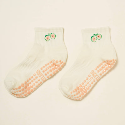The Effortless Club Fig Cropped Crew Grip Socks are white Pilates socks with peach motifs near the top and light pink non-slip soles, shown on a plain light background.
