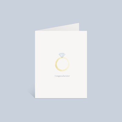 The Korynne and Company Engagement Ring Greeting Card features a gold diamond ring illustration and “Congratulations!” on textured felt A2 paper, shown with a white Euroflap envelope against a light gray backdrop.