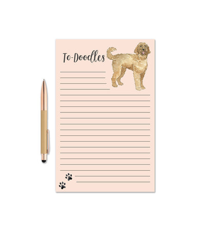 The Golden Doodle Dog Notepad - Watercolor Notepad by KelseyMDesigns features lined pages, a doodle dog illustration at the top right, black paw prints at the bottom, and comes with a gold pen. Perfect for dog lovers!.
