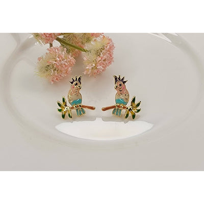 BETTYOH INC Parrot Post Earrings feature gold-tone colorful parrots perched on green branches, accented with sparkling cubic zirconia and titanium posts. Shown on a white dish with pink flowers in the background.