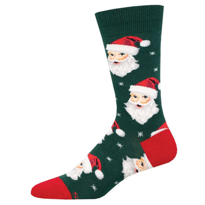 The Socksmith Santa Men's Socks in size 10-13 are green crew socks featuring red heel and toe, festive Santa faces in red hats, white snowflakes, and are made from soft cotton for comfort.
