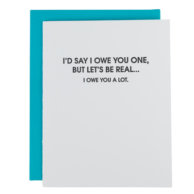 The Chez Gagné Let’s Be Real, I Owe You A Lot Thank You Card is a bright white folded card with bold black text, made from tree-free paper, shown atop a blue envelope.
