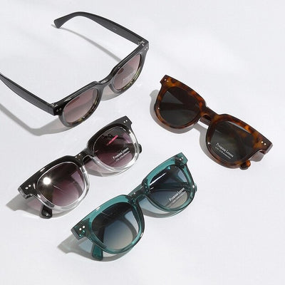 Four pairs of Fashion City’s Sloan Sunglasses are displayed on a white surface with colored gradient lenses. Available in black, tortoiseshell, clear with black accents, and teal, each stylish pair offers UV protection, blending fashion and function with their dark-tinted elegance.