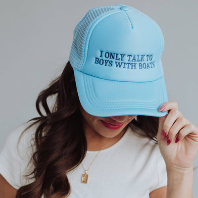 Someone with long brown hair, red lipstick, a white shirt, and a gold pendant necklace is wearing Panache Apparel Co.s Boys With Boats Trucker Hat in light blue, featuring the embroidered text I ONLY TALK TO BOYS WITH BOATS and an adjustable snapback closure.