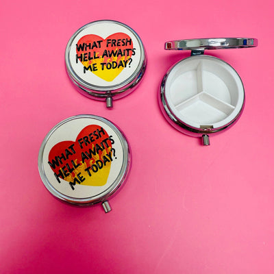 Three Sonny Rising Purse Pill Boxes read "What Fresh Hell Awaits Me Today?" on the lids. Two are closed to show the design; one is open, revealing three compartments—great for travel pills. A bright pink background adds flair.
