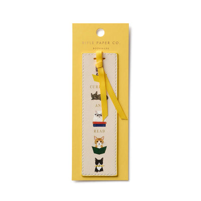 The Studious Cats Bookmark by Rifle Paper Co. features cat illustrations reading books with Curl Up And Read on a cream background, attached to a yellow card and finished with a yellow grosgrain ribbon.