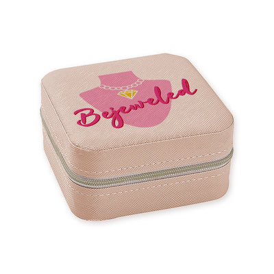 The Bejeweled Travel Jewelry Box (Blush) by Toss Designs is a square, beige zippered case crafted from vegan leather with a textured surface. It features multiple compartments and has a lid adorned with a pink necklace silhouette and the word Bejeweled in elegant pink script. Perfect for travel!.