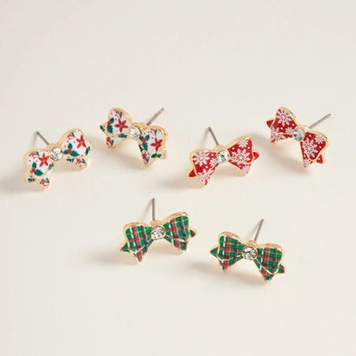 The Golden Stella Christmas Bow Patterned Earrings set includes three pairs of 0.5-inch stud earrings with festive red and green plaid, snowflake, and floral designs, each featuring a sparkling gem center. Made in China from zinc.