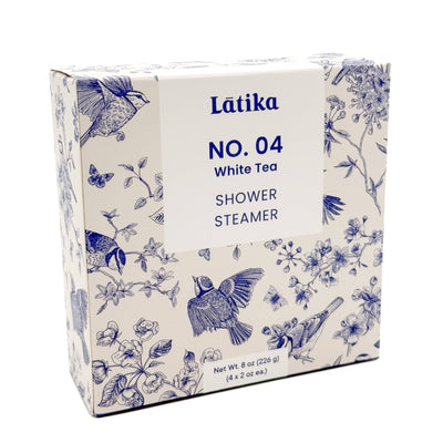 A box of Latika Beautys Chinoiserie White Tea Shower Steamers - 4 pack offers a spa-like experience at home. The packaging showcases a white background with blue bird and flower illustrations, labeled with a net weight of 8 oz (226 g), containing four 2 oz fragrance-infused tablets.