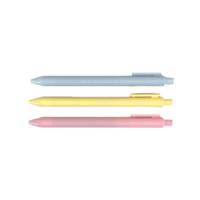 The Pens for New Moms by Tiny Hooray are lined up horizontally: blue says Able to Function on Minimal Sleep, yellow reads Expert Late Night Googler, and pink declares So Happy / So Tired. Each one writes with smooth black gel ink.