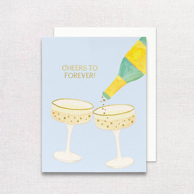 Gert & Co’s “Champagne Wedding Greeting Card | Cheers to Forever” features a green and yellow champagne bottle pouring into gold star-patterned flutes, with “Cheers to forever!” in gold—ideal for celebrating any wedding.