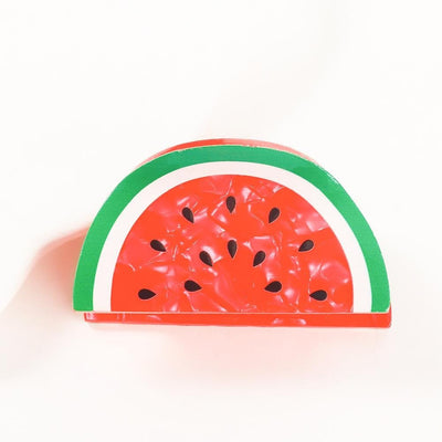 The Watermelon Slice Hair Claw Clip by Judson & Company is a small accessory shaped like a watermelon slice, featuring a red textured surface with black seeds and green and white striped edges, perfectly capturing the fruits essence on a plain white background.