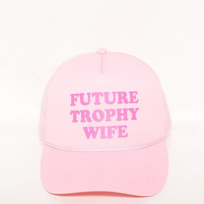 The Judson & Company Future Trophy Wife Trucker Hat in pink showcases bold pink lettering on a white backdrop. Made from 100% cotton, it provides comfort with its snap back closure, fitting most sizes.