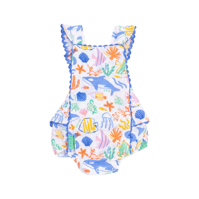 The Colorful Reef Ric Rac Ruffle Sunsuit by Angel Dear features blue whales, orange starfish, shells, and coral on soft bamboo viscose with added spandex. It has ruffled straps and blue scalloped trim on a white background.