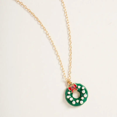 The Golden Stella Christmas Wreath Necklace features a zinc pendant shaped like a green wreath with white pearls and a red bow, hanging from an 18-inch gold chain.