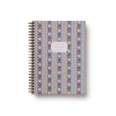 The Delphine Spiral Notebook by Rifle Paper Co. features a blue cover with pink, yellow, and green floral and zigzag designs, a central white "NOTEBOOK" label, and ruled pages for neat writing.