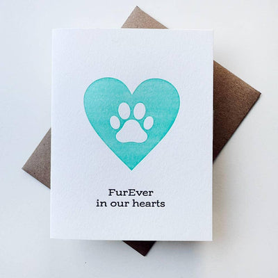 The FurEver In Our Hearts Pet Sympathy Card by Steel Petal Press is a handmade white card with a turquoise heart and white paw print, letterpressed with “FurEver in our hearts,” and comes with a brown envelope.