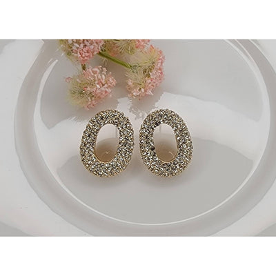 The BETTYOH INC Oval Rhinestone Post Earrings feature a gold-tone oval design with sparkling crystals. Lead & nickel free, these elegant earrings are shown on a white surface with pink flowers in the background.