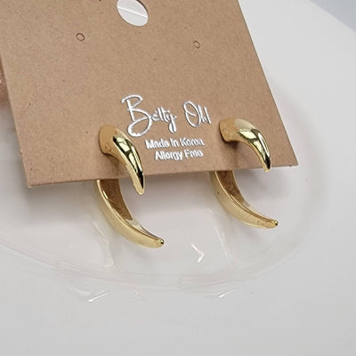 A pair of Thorn Ear Jacket Earrings by BETTYOH INC, gold and claw-shaped with titanium posts, sits on a brown card labeled “BETTYOH INC, Made in Korea, Allergy Free” atop a white surface.