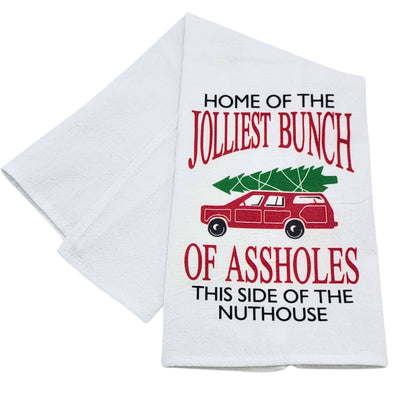 The Driftless Studios "Home Of The Jolliest Bunch Christmas Tea Towel" is a crinkled cotton flour sack towel, printed in the USA, featuring a red car with a tree and bold, funny text. Machine washable for easy care.