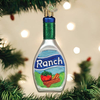 The Old World Christmas Ranch Dressing Ornament, shaped like a ranch dressing bottle, hangs on a tree branch amid green needles and festive lights.