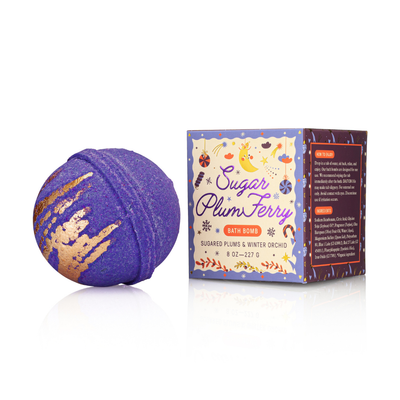 A purple and gold Sugar Plum Ferry Bath Bomb by Old Whaling Company rests beside its festive box, making it a perfect holiday gift with the scent of sugared plums and winter orchid.