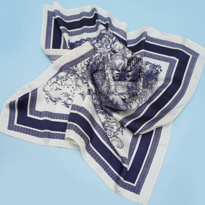 The LARGE FLORAL TOILE PRINT BANDANA SCARF by JOSSLYN features navy and white floral patterns on light blue, making it an elegant choice for a womens scarf or fashion bandana.