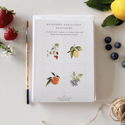 Fruit paintable notecards by emily lex studio rest on a white surface with a paintbrush, twine, fruit, and greenery nearby—ideal for crafting your own custom DIY greeting cards.