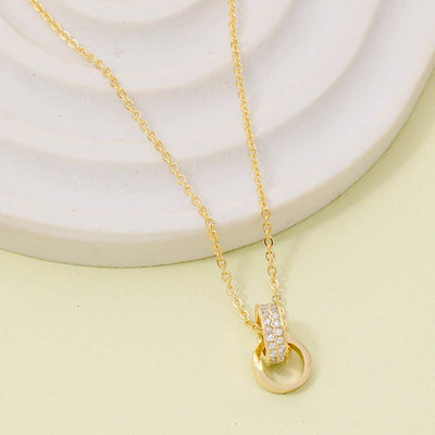 The Fame Accessories CZ Double Ring Link Pendant Necklace features a gold-dipped design with one plain and one crystal-encrusted ring, elegantly displayed on a white textured surface. Modern and beautifully crafted in Korea.
